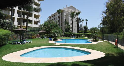 Gemeinschaftspool-Bereich mit Sonnenliegen, Sonnenschirmen und Palmen